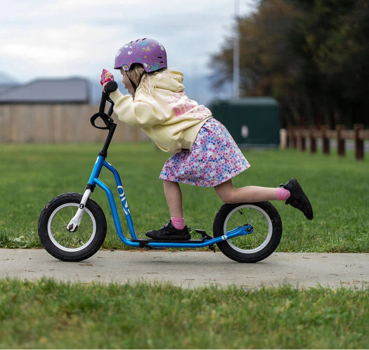 Child riding a balance bike on a sidewalk with grass and houses in the background